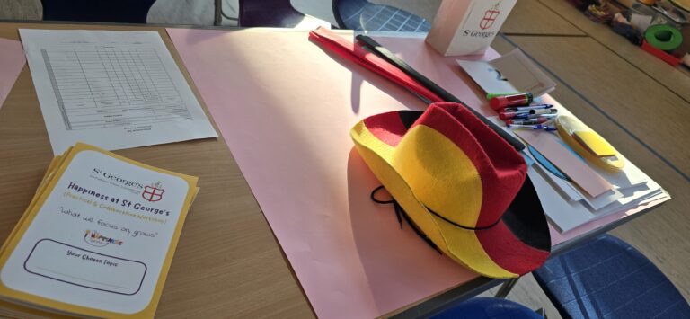 Image of one of the tables before an Appreciative Inquiry workshop. There is a booklet (Appreciative Inquiry Interview Guide), various sizes and colours of paper, a colourful hat, crêpe paper, felt tip pens, scissors, glue, colourful pipe cleaners etc.